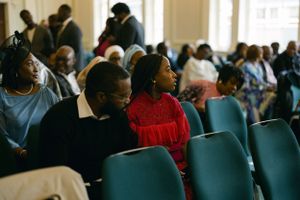 Congregation members seated in teal chairs during church service.