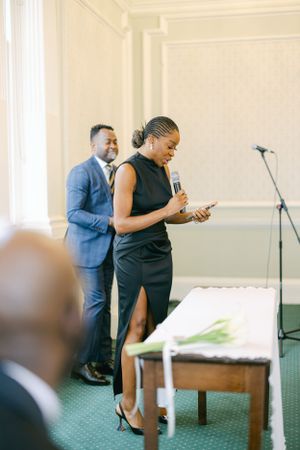 Speaker in elegant black dress stands at podium during formal event.