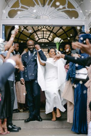 Joyful newlyweds exit their wedding venue while guests shower them with confetti.