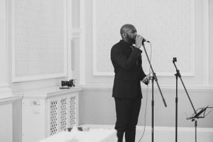 Performer in black suit singing at microphone during event.