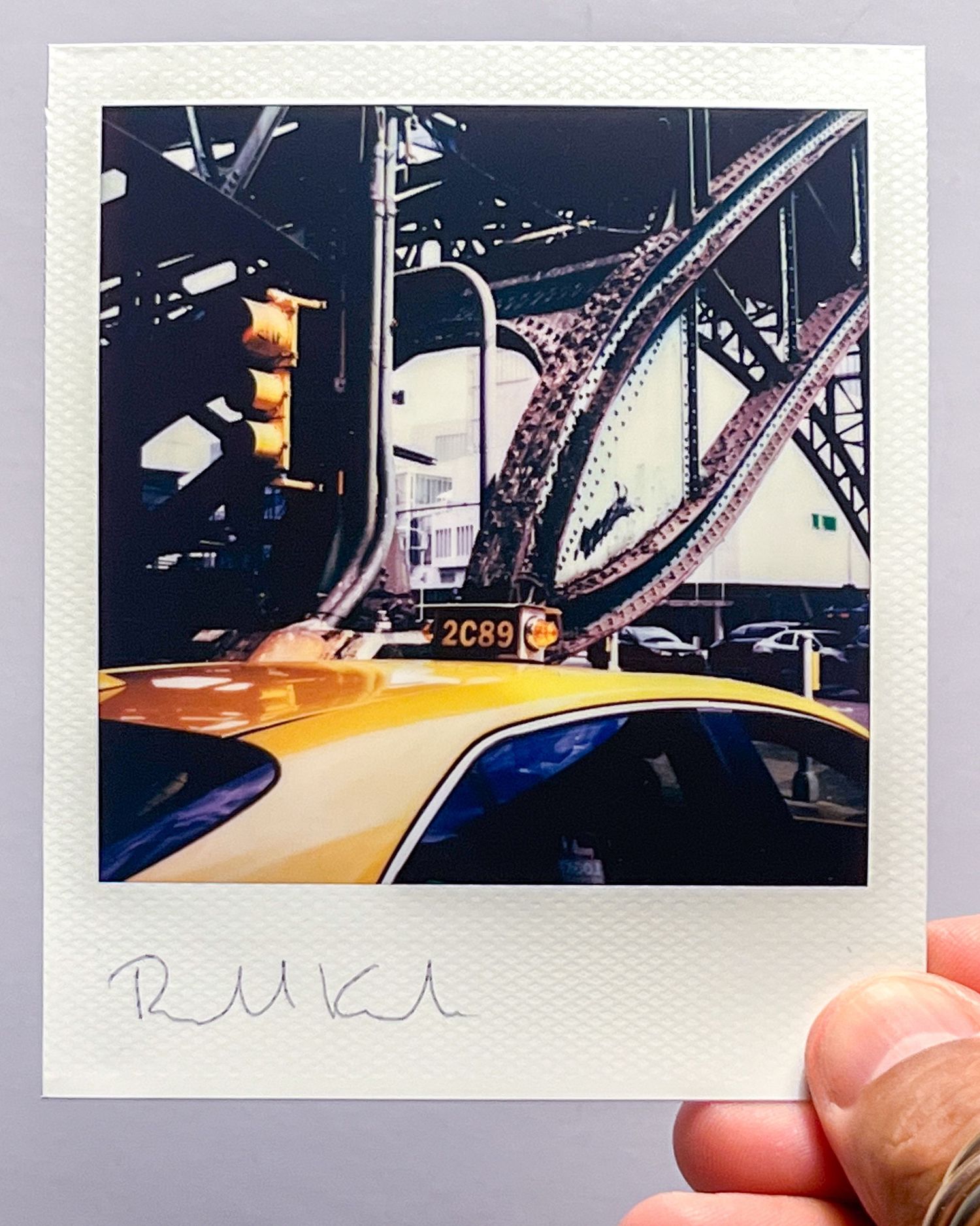 Polaroid photo of a yellow taxi with Brooklyn Bridge in background.