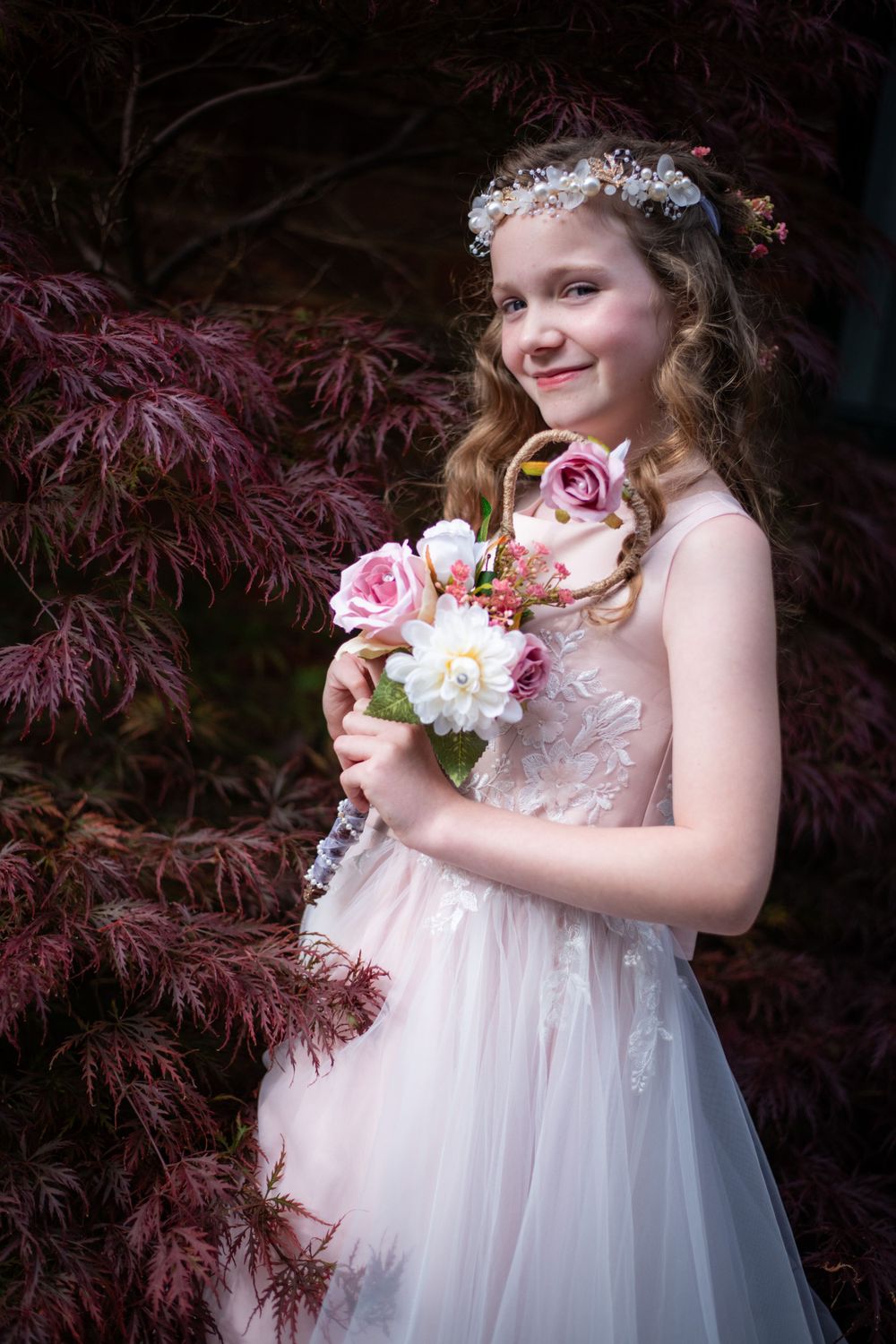 Ethereal portrait with floral crown and bouquet against purple Japanese maple leaves.
