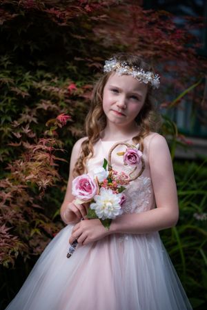Elegant portrait in pink tulle gown holding roses against Japanese maple background.