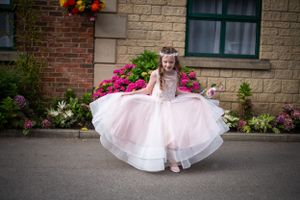 An ethereal pink and white flower girl dress twirls against a backdrop of vibrant pink flowers.