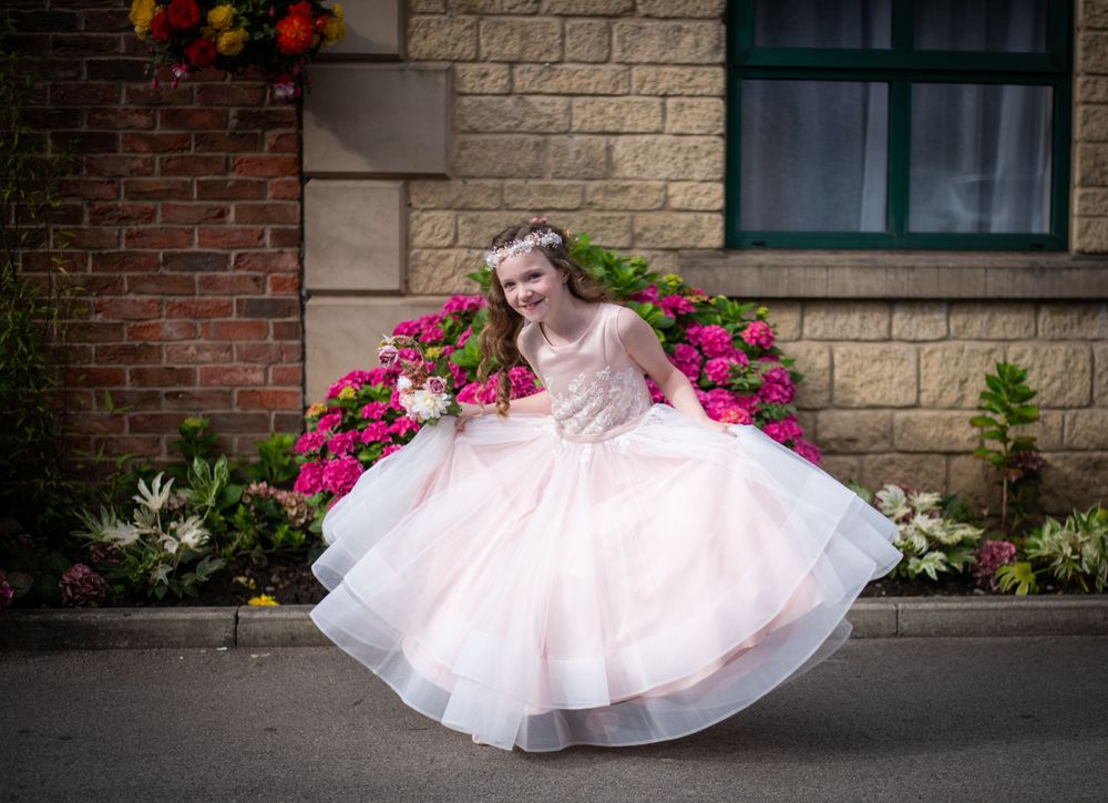 A whimsical scene of a twirling dress against a stone wall with bright pink flowers.