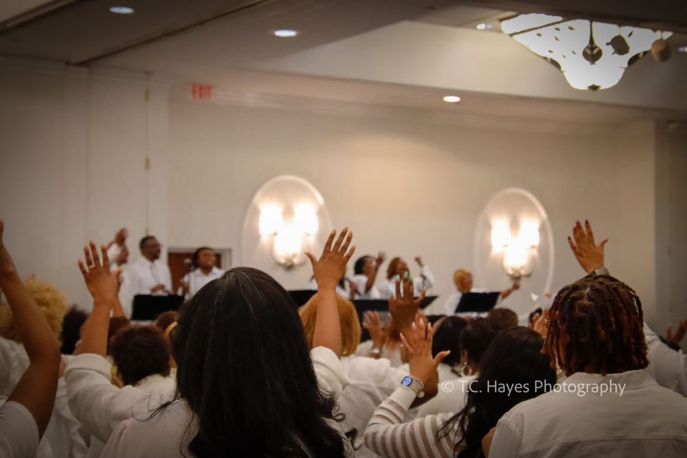 People with raised hands during worship service in a room with glowing wall sconces.