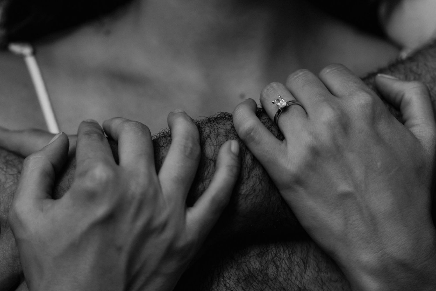 Close-up black and white photo of hands with rings intertwined.