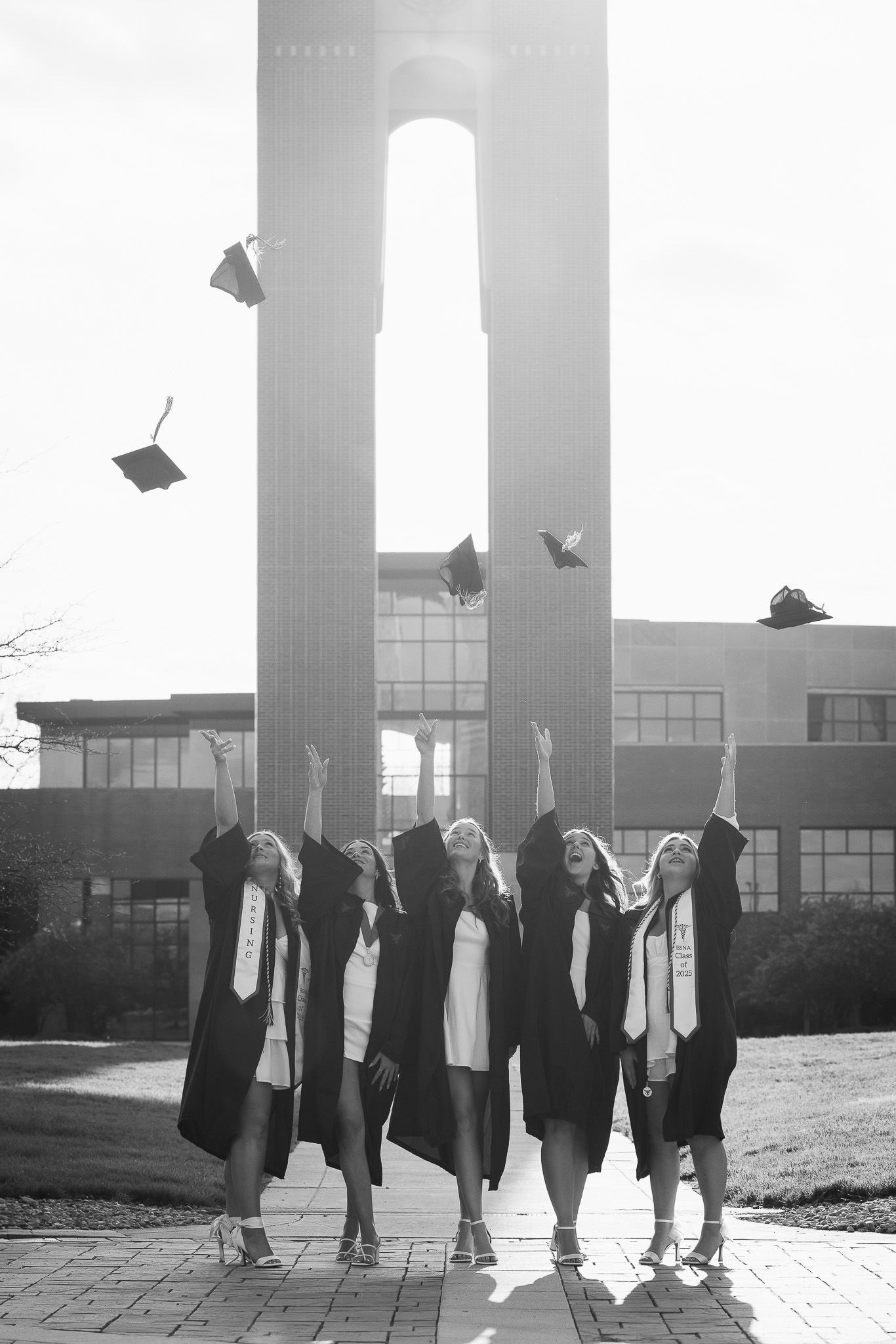 Black and white photo of graduates throwing caps in celebration outside a building.