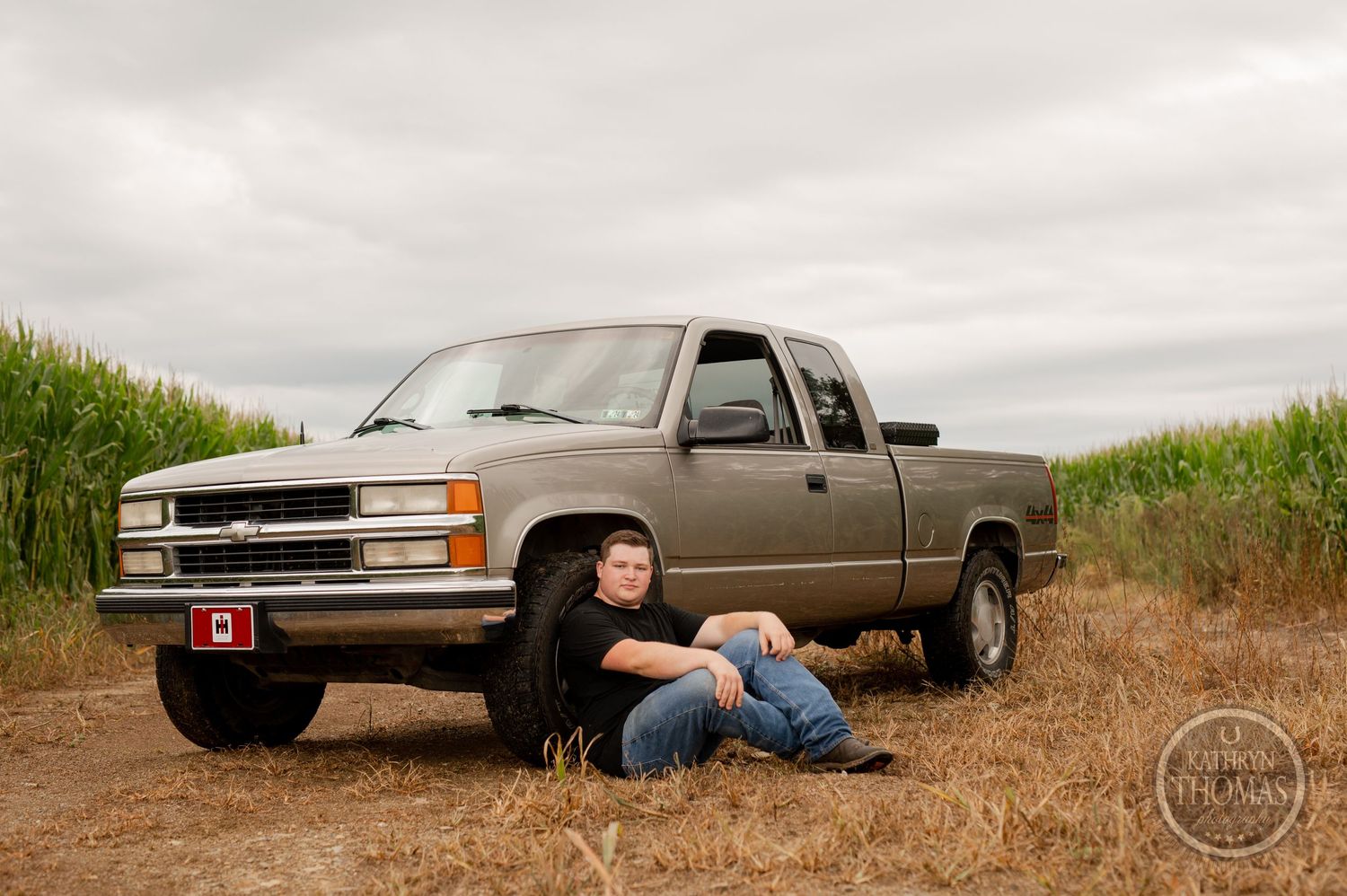 A classic Chevrolet pickup truck parked between cornfields with someone sitting beside it.