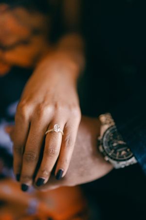 Close-up of a sparkling engagement ring on a hand with dark nail polish.