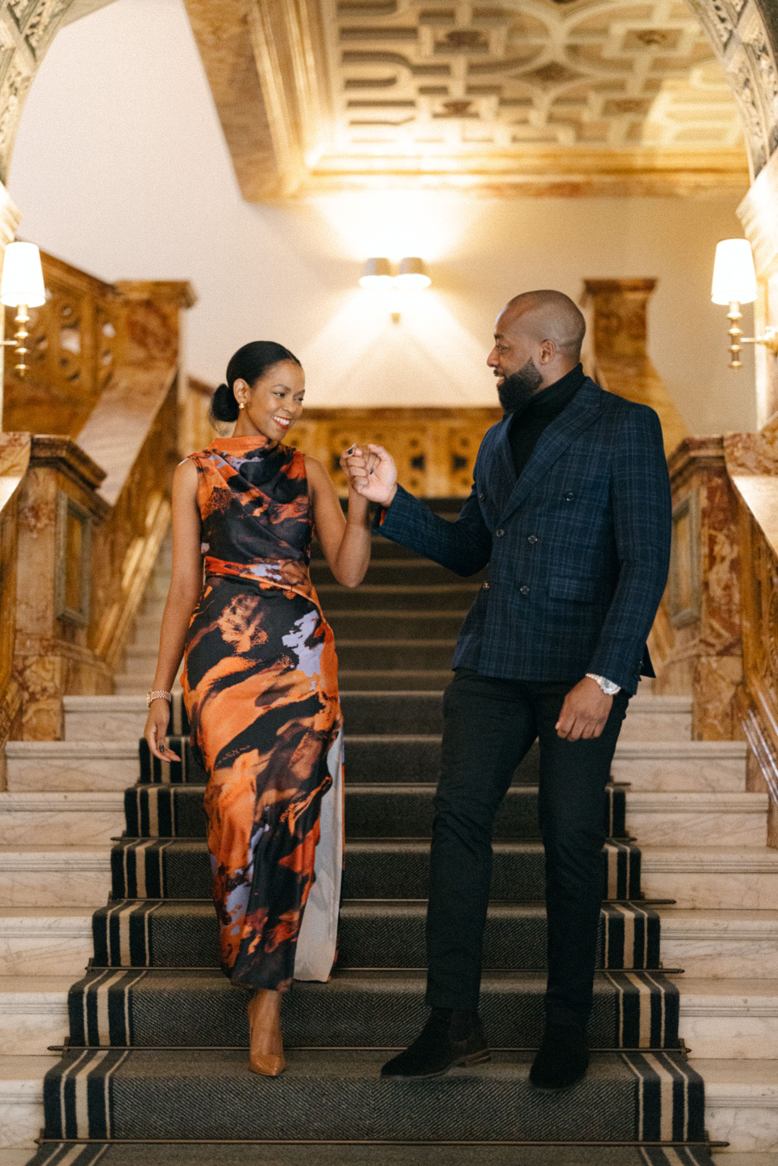 A couple dances together on an ornate staircase in a historic building interior.