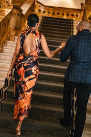 A couple ascends a grand staircase together, with elegant formal attire and architectural details.
