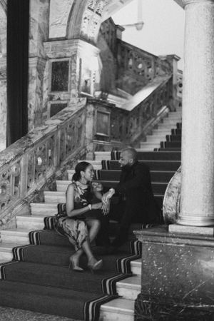 A couple sits together on grand carpeted stairs in a vintage black and white photo.