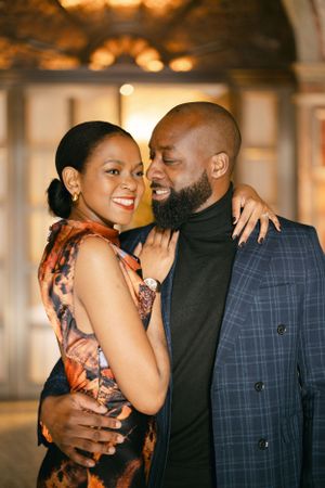 A romantic couple shares laughter in an elegant venue, dressed in formal attire.