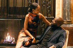 A couple shares an intimate moment in front of a fireplace in a luxurious setting.