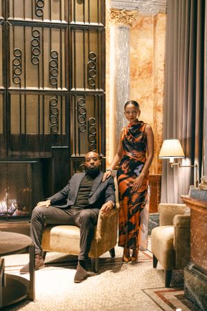 A couple poses elegantly in a vintage-inspired interior with ornate metalwork and warm lighting.