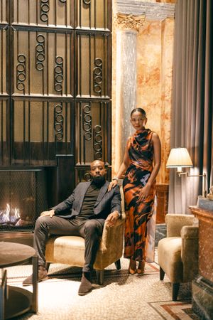 A stylish couple poses in an elegant room with ornate iron gates and warm lighting.