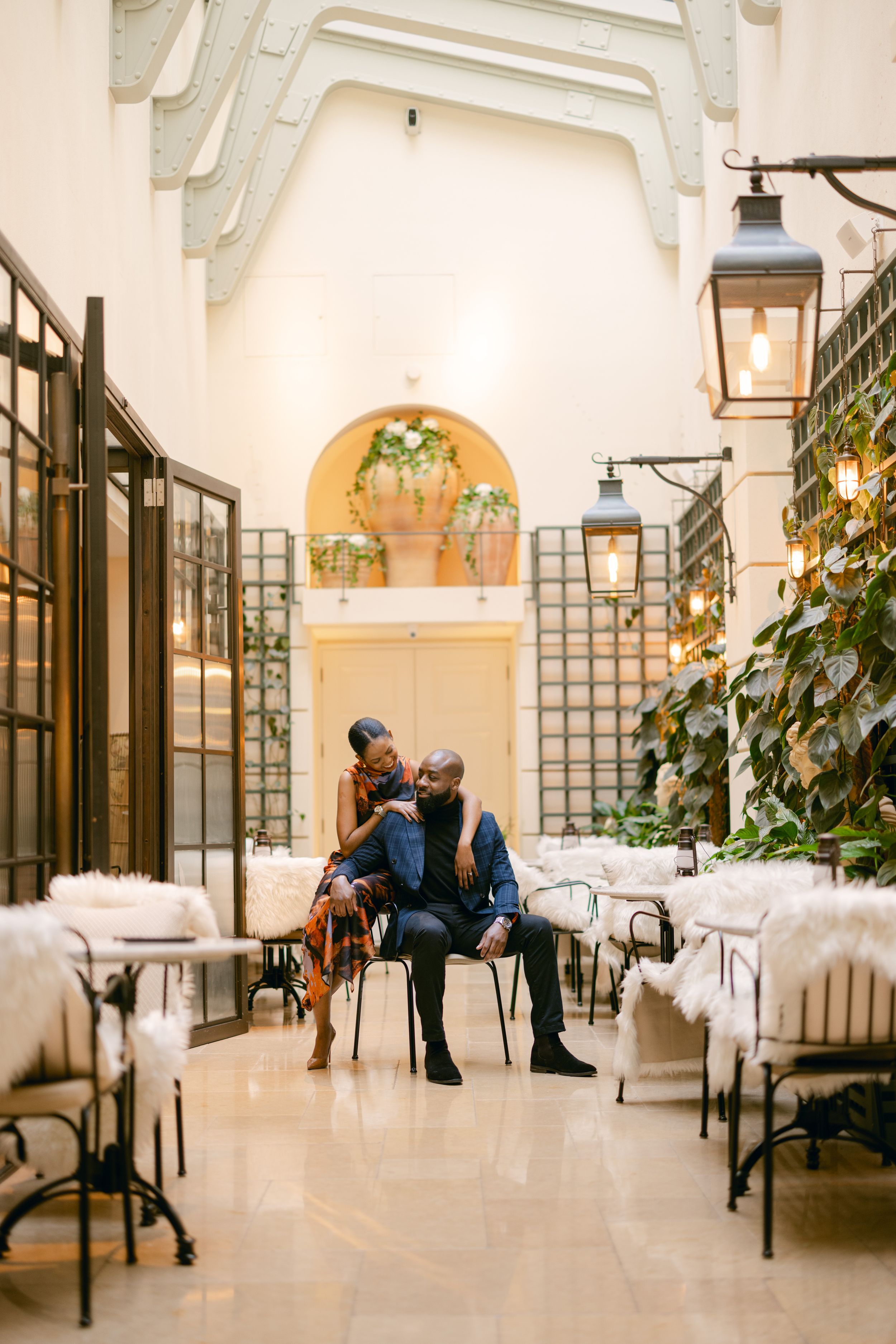 A couple shares a romantic moment in an elegant restaurant with white decor and hanging lanterns.
