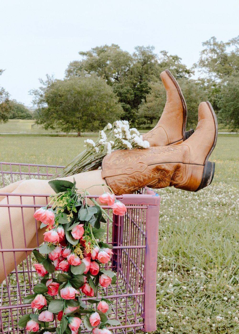 Brown leather boots displayed on pink metal fence with pink roses and greenery.