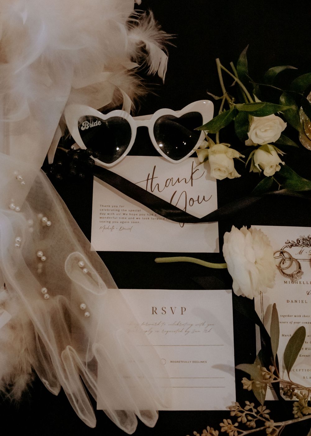 Wedding invitation suite with white feathers, roses and elegant calligraphy on black background.