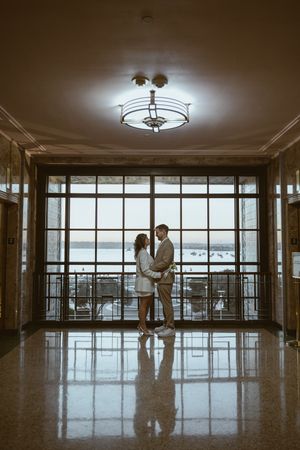 Intimate moment captured in a spacious room with large windows and dramatic lighting.