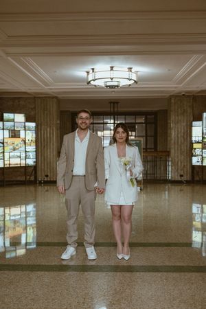 Couple in coordinated outfits standing in an elegant lobby with detailed ceiling.