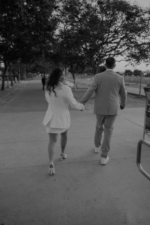 Black and white shot of couple walking away on pathway surrounded by trees.