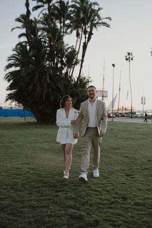 Couple walking together on a grassy lawn with palm trees at sunset.