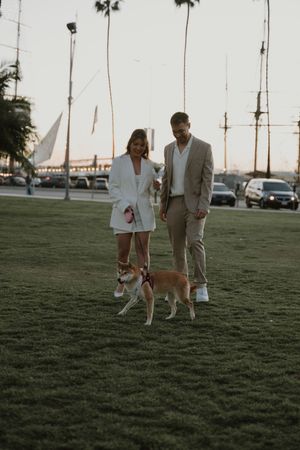 Couple and their dog enjoying a stroll on grass near palm trees at dusk.