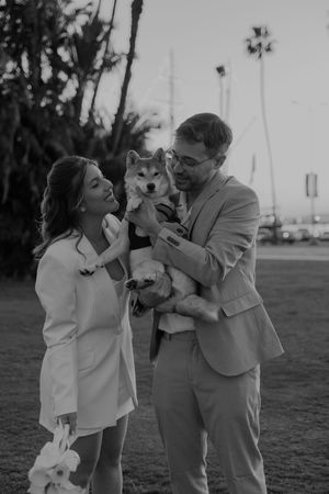 Black and white photo of a couple playing with their dog on a grassy field.