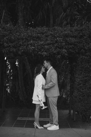 Black and white photo of a couple sharing an intimate moment in a garden setting.