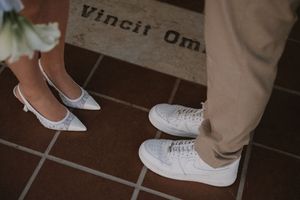 Close-up shot of white sneakers and dress shoes on tiled floor.