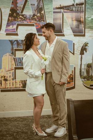 Couple in matching light suits posing against LA themed backdrop with city landmarks.