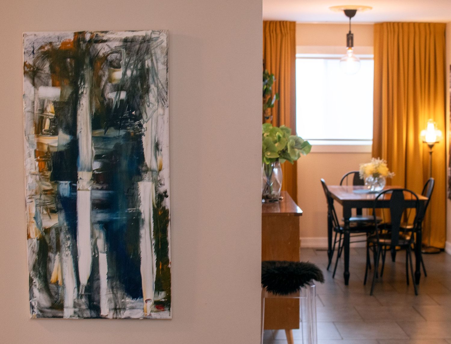 Modern interior with abstract blue artwork and dining area with orange curtains.