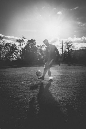 Silhouette of a soccer player practicing with a ball in dramatic sunlight.