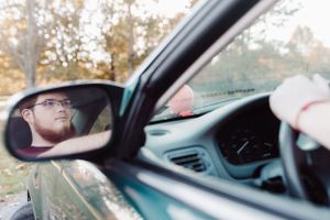 View of someone through a car side mirror while driving at sunset.