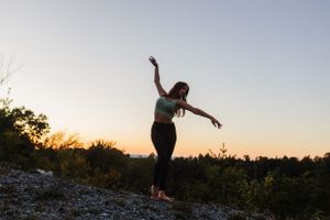 A dancer performs graceful movements on a rocky outcrop during sunset.
