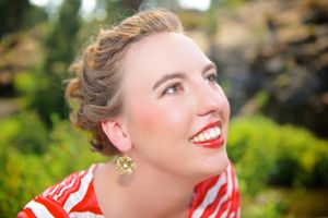 Portrait of woman with red lipstick and updo hairstyle glancing upward in garden setting.