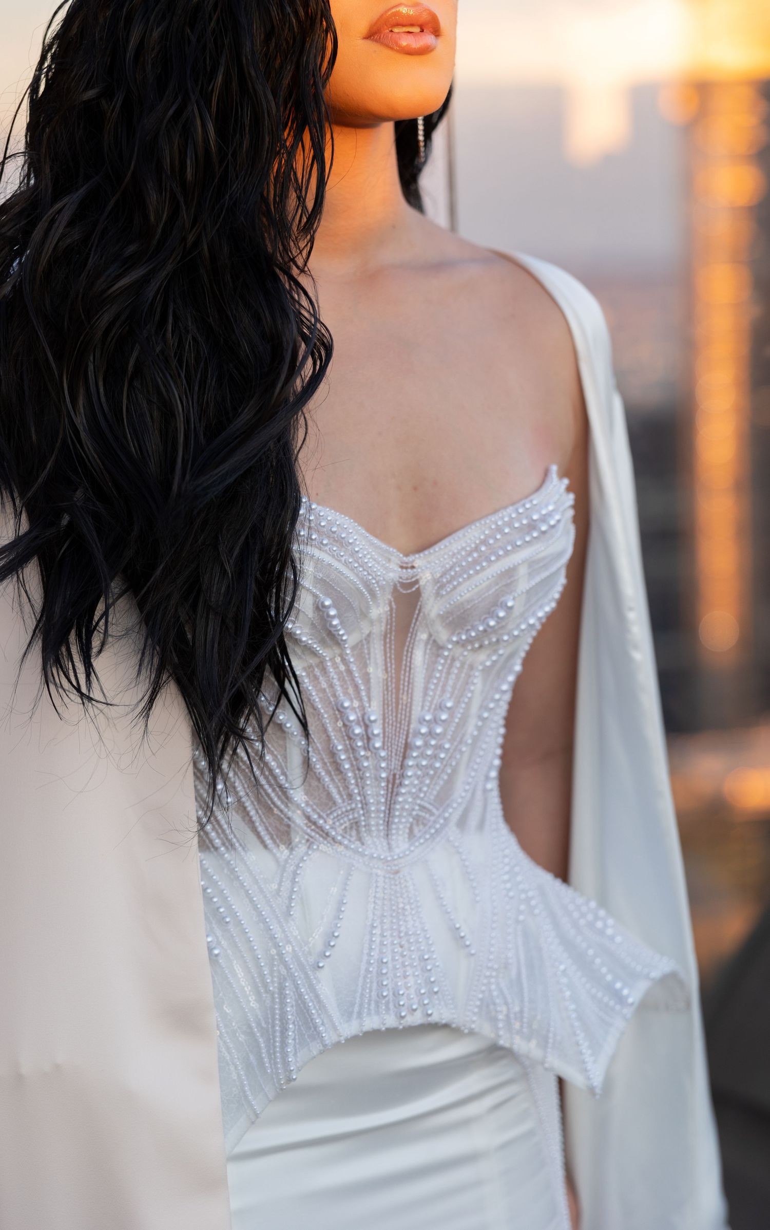 Close-up of intricate beaded white wedding dress bodice in sunset lighting.