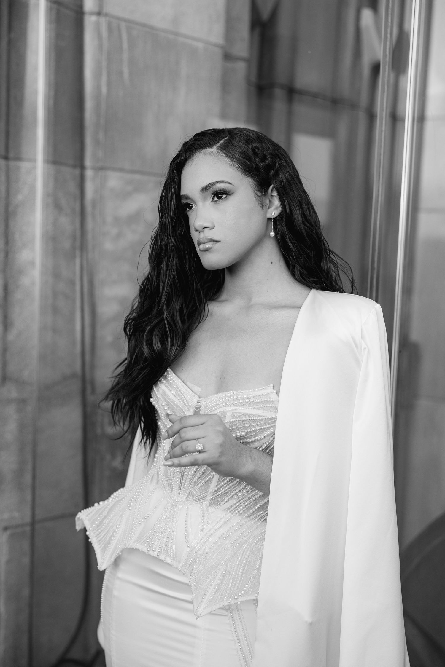Portrait of woman in white corset dress against stone column in black and white.