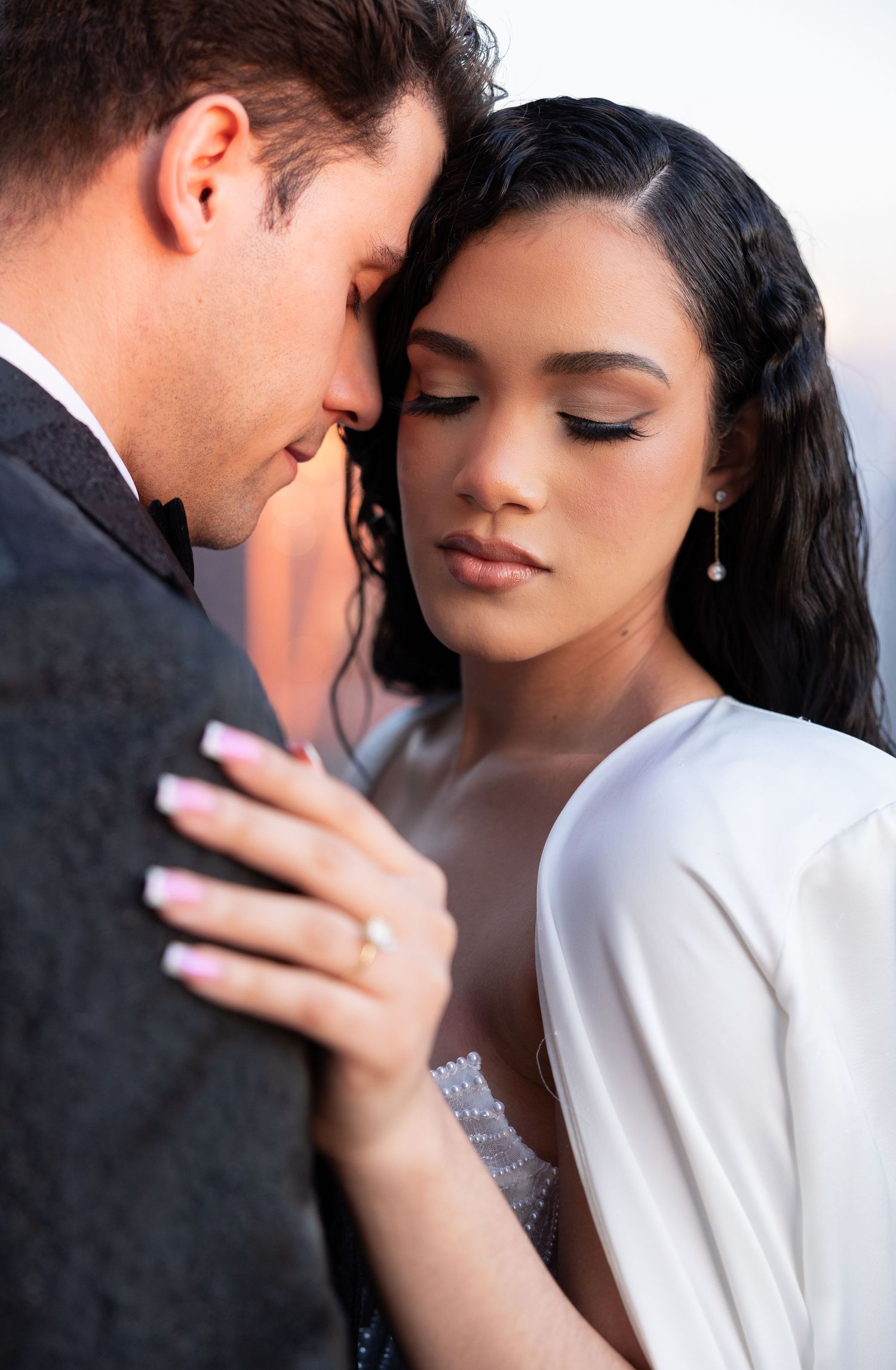A romantic wedding portrait showing a tender intimate moment between a couple in formal attire.