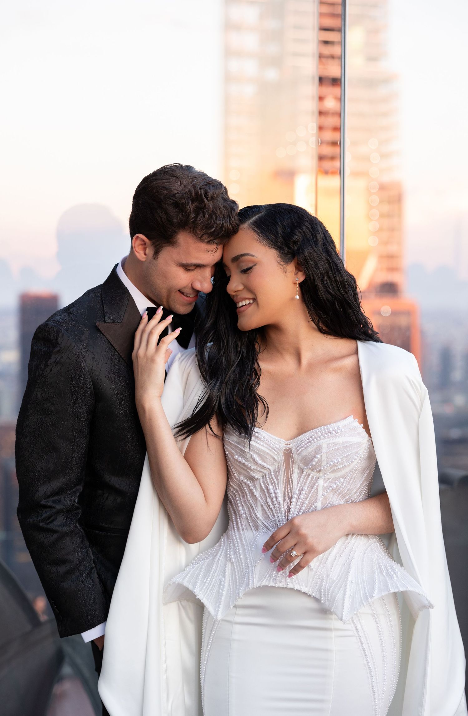 Newlyweds share an intimate moment on a rooftop with city buildings in the background at sunset.
