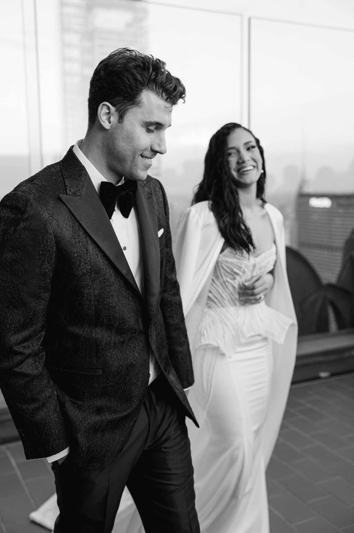 Black and white wedding photo of a couple laughing together on a rooftop terrace.