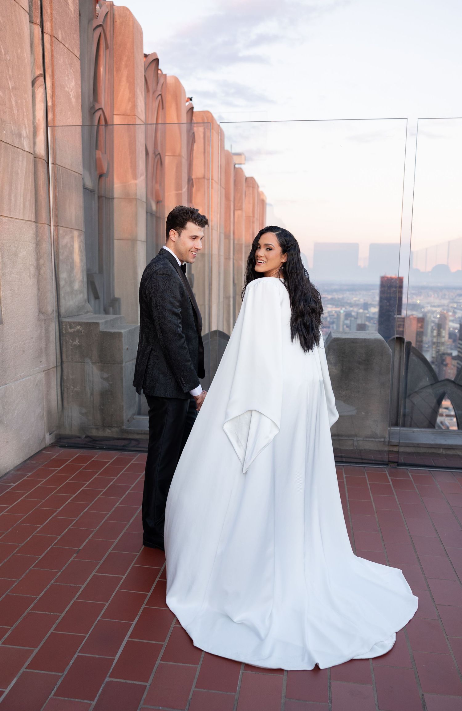 Wedding couple poses on a rooftop terrace with terracotta walls and city views.