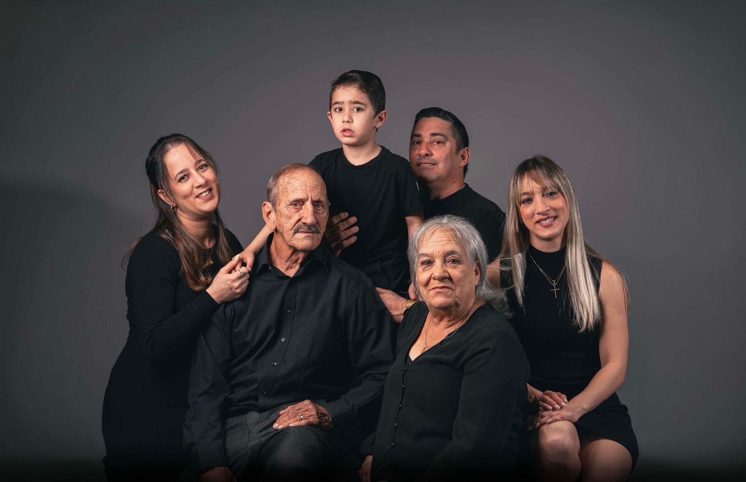 Studio family portrait of multi-generational group in black attire against grey background.