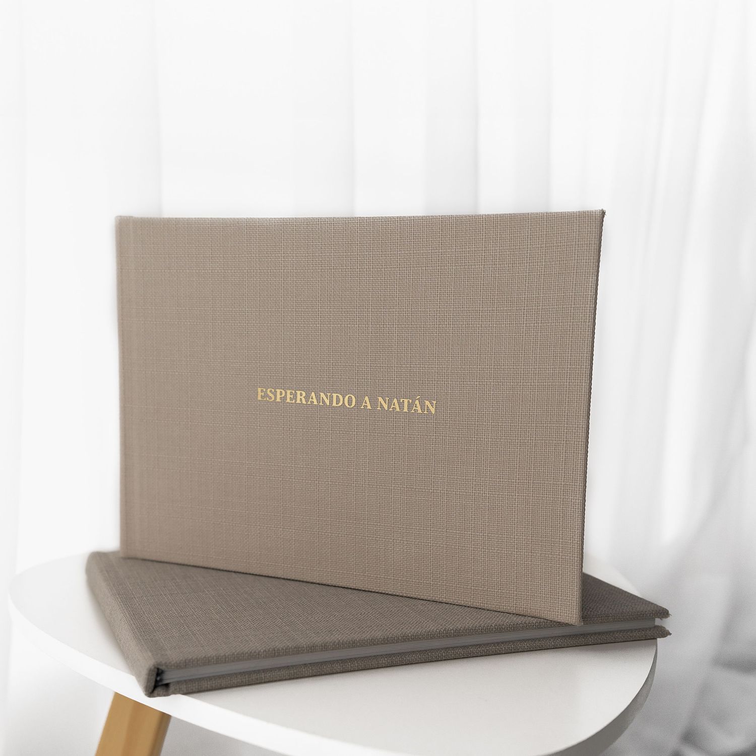 Taupe colored photo album with gold text on white surface.