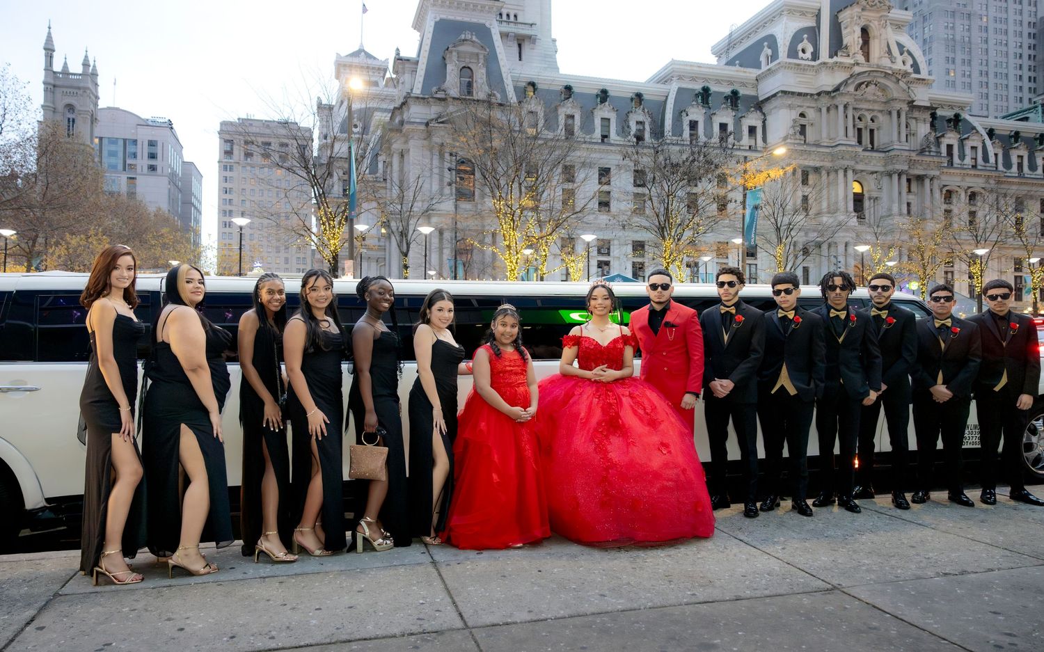 A formal group photo showing bridesmaids in black and a central figure in red against historic architecture.