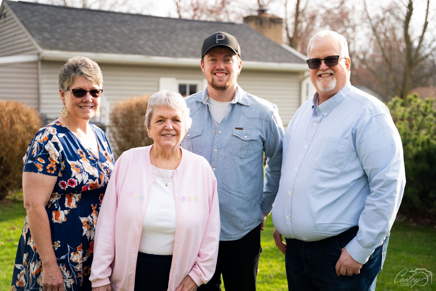Group of four people smiling together outdoors in front of a residential home in spring.