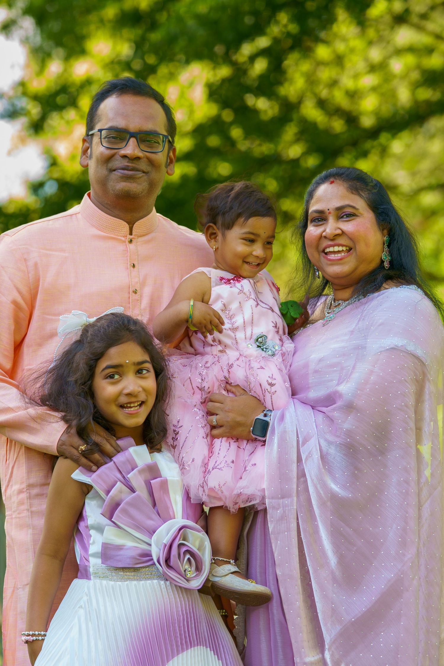 Happy Indian family of four in traditional pink attire posing together in a sunny green park.