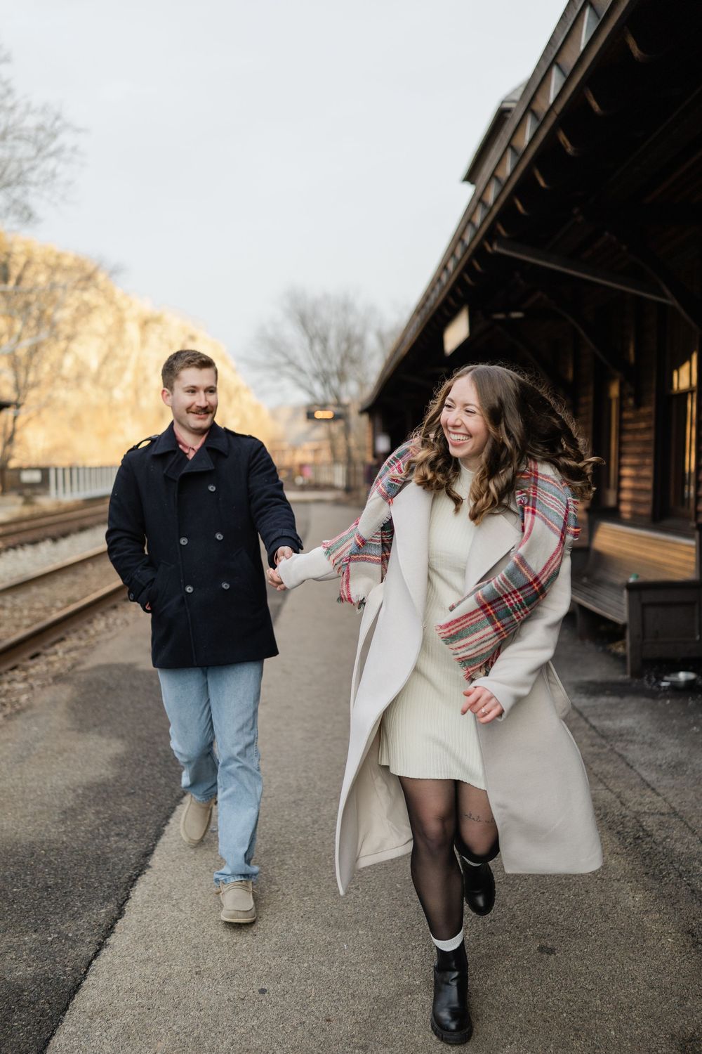 A couple walking and laughing together on a train platform during a winter engagement photo session.